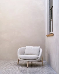 White textured armchair with a matching throw pillow on a tiled floor against a neutral stucco wall by Sigurd Kranendonk