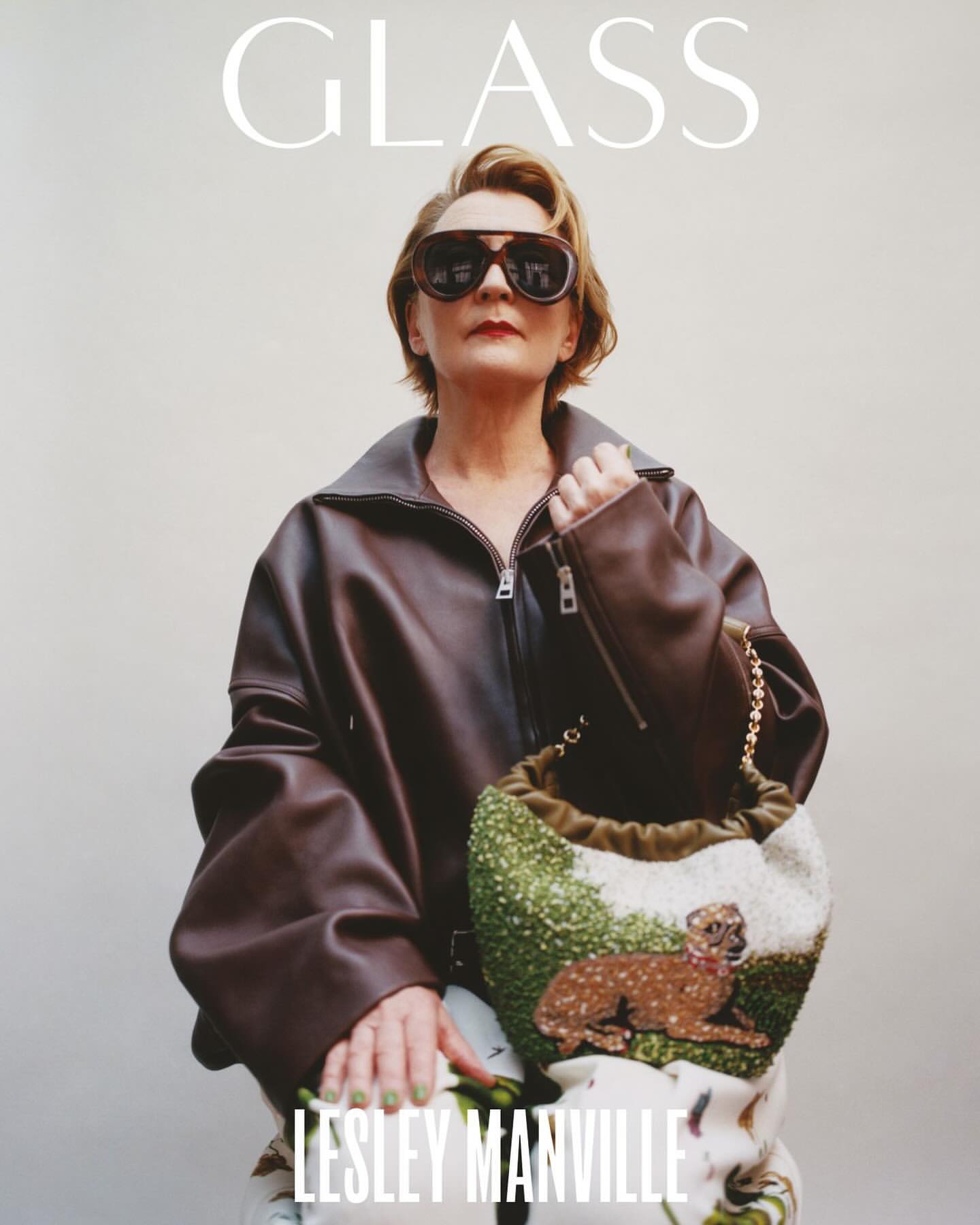 Lesley Manville poses in a brown leather jacket, patterned pants, and oversized sunglasses holding a beaded bag for Glass magazine.
