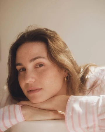 Portrait of a woman resting her head on her hands wearing pink striped sleepwear, photographed by Silvana Trevale.