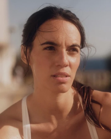 Close-up portrait of a woman with dark hair wearing a white top outdoors in natural sunlight by Silvana Trevale