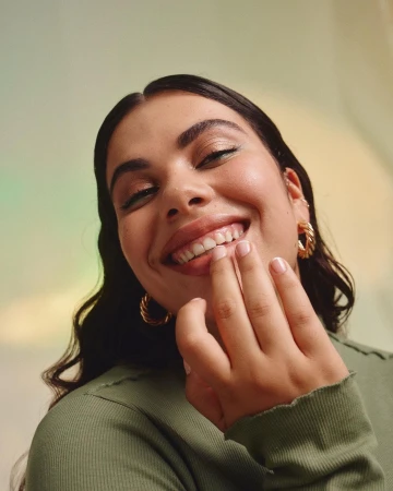 Close-up portrait of a smiling woman in a green ribbed top with gold hoop earrings by photographer Silvana Trevale.