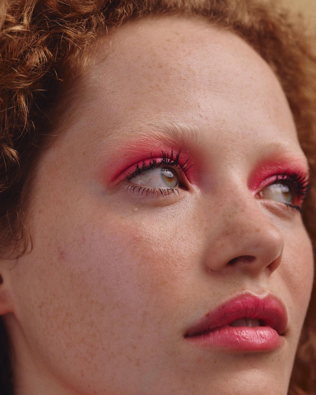 Close-up portrait of a woman with curly red hair, bright pink eyeshadow, and freckles photographed by Silvana Trevale.
