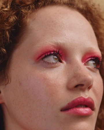 Close-up portrait of a woman with curly red hair, bright pink eyeshadow, and freckles photographed by Silvana Trevale.