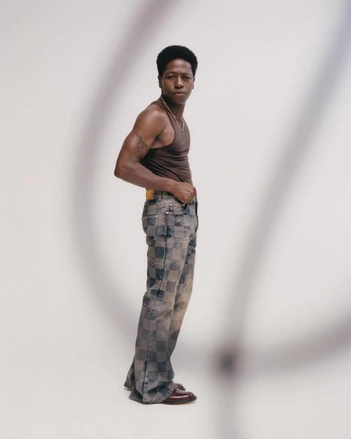 Man in tank top and patterned pants posing in a photo studio with soft lighting and shadows creating an editorial fashion portrait.