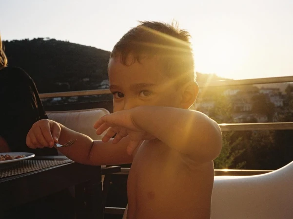 Young child holding up a fork while seated outdoors at sunset with hills visible in the background.