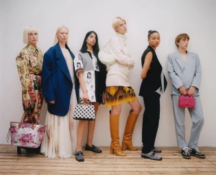 Six models posing in contemporary designer outfits against a plain white wall with a wood floor, photographed by Silvana Trevale.