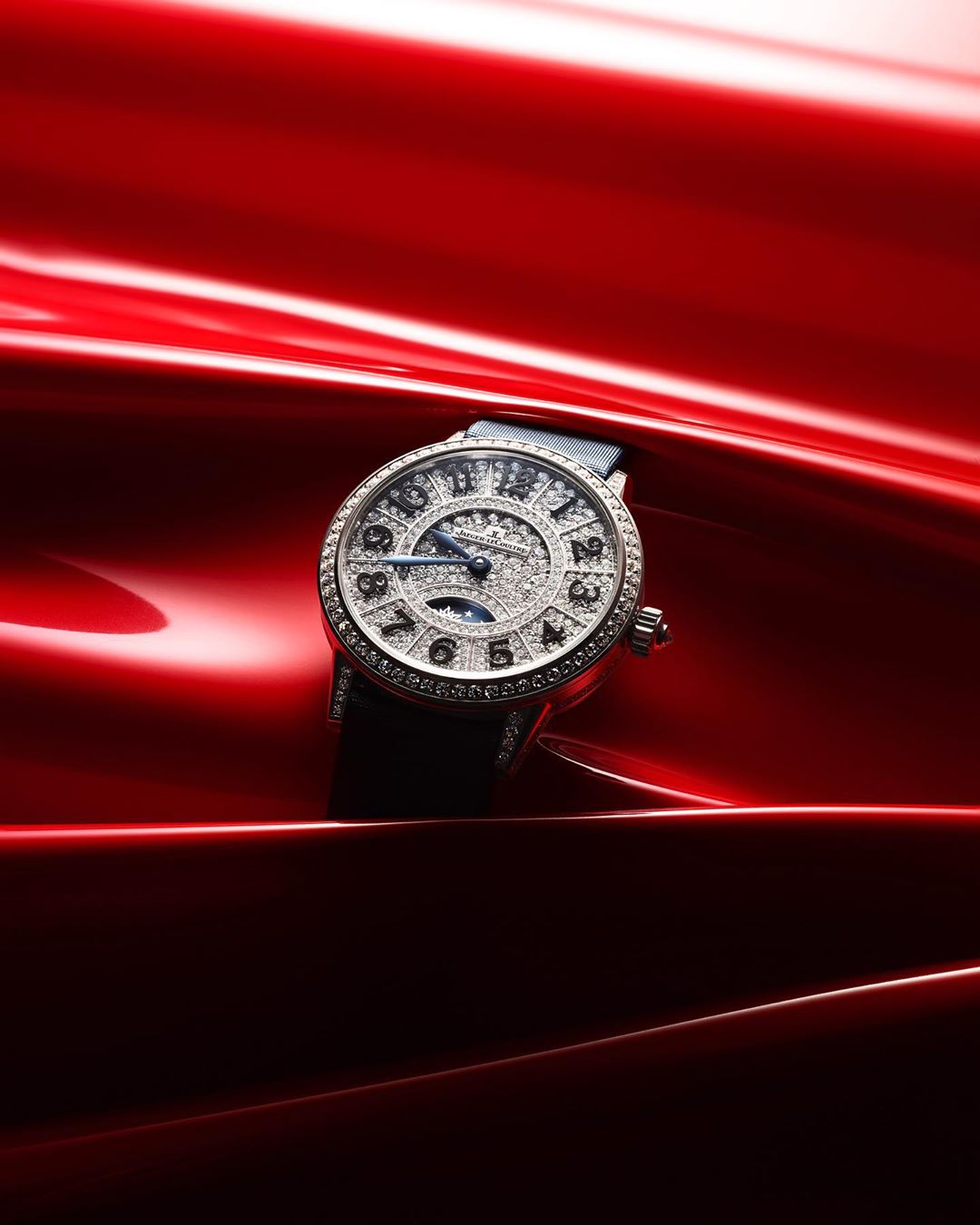 Luxury wristwatch with diamond embellishments on a red satin background, highlighted by soft lighting that accentuates its elegance.