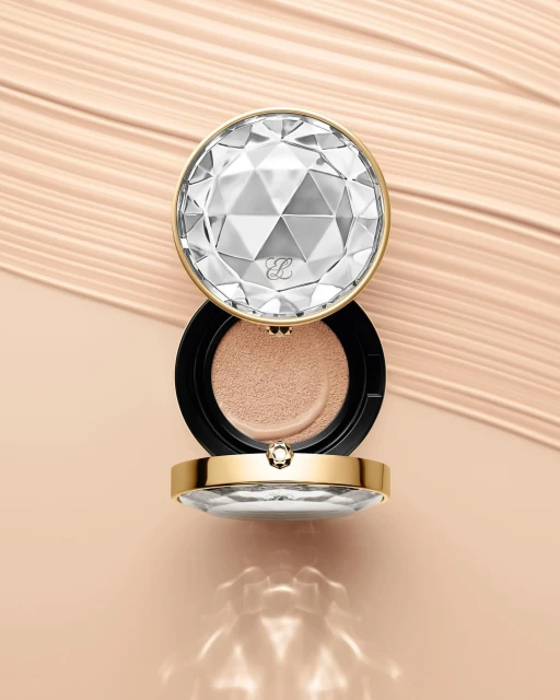 Elegant makeup compact featuring a faceted, diamond-like lid, accented with gold trim, displayed against a cosmetic cream background.
