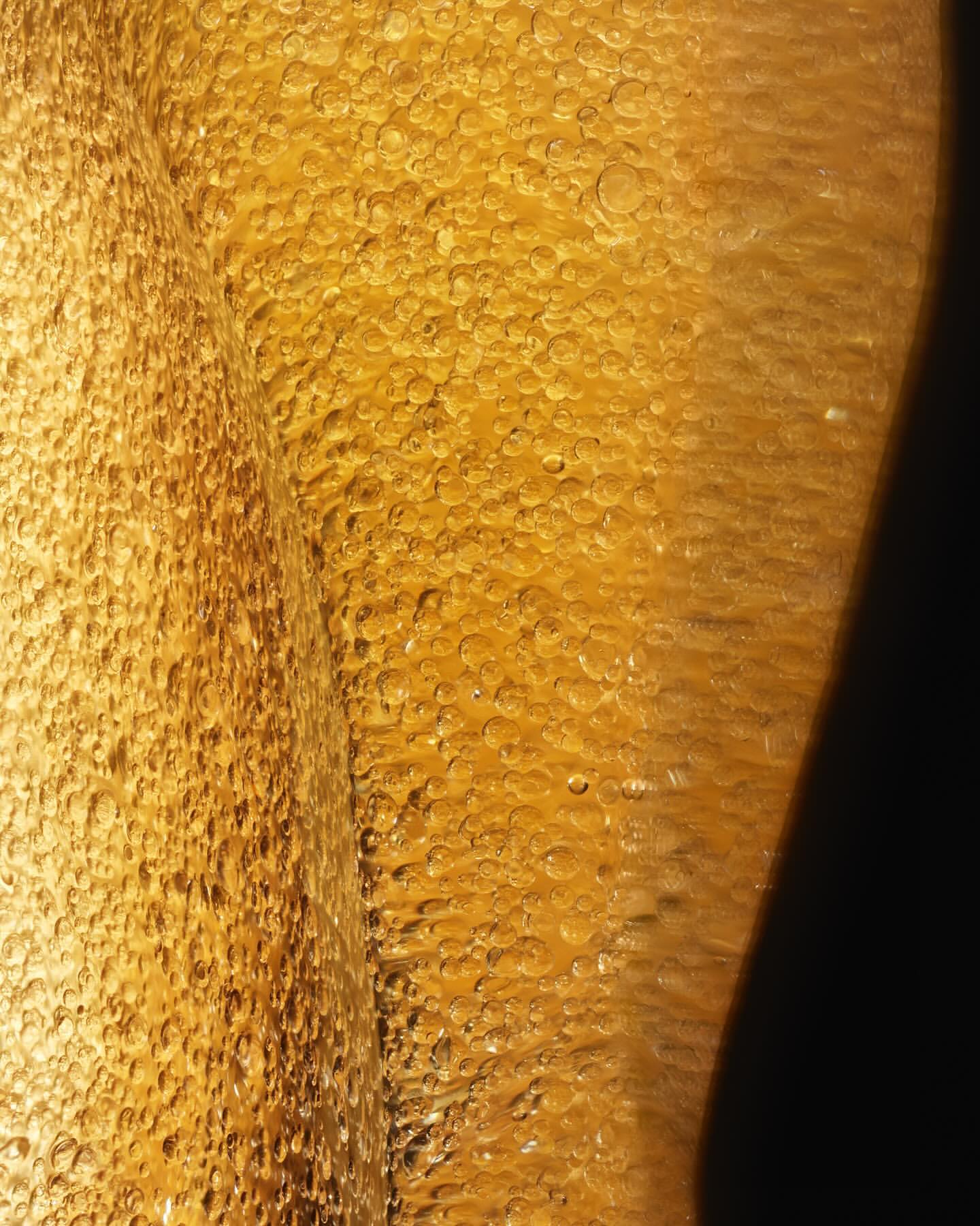 Close-up view of light shining through golden liquid with bubbly texture, creating a rich, textured surface with highlights and shadows.