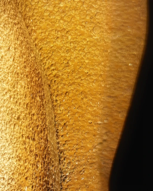 Close-up view of light shining through golden liquid with bubbly texture, creating a rich, textured surface with highlights and shadows.