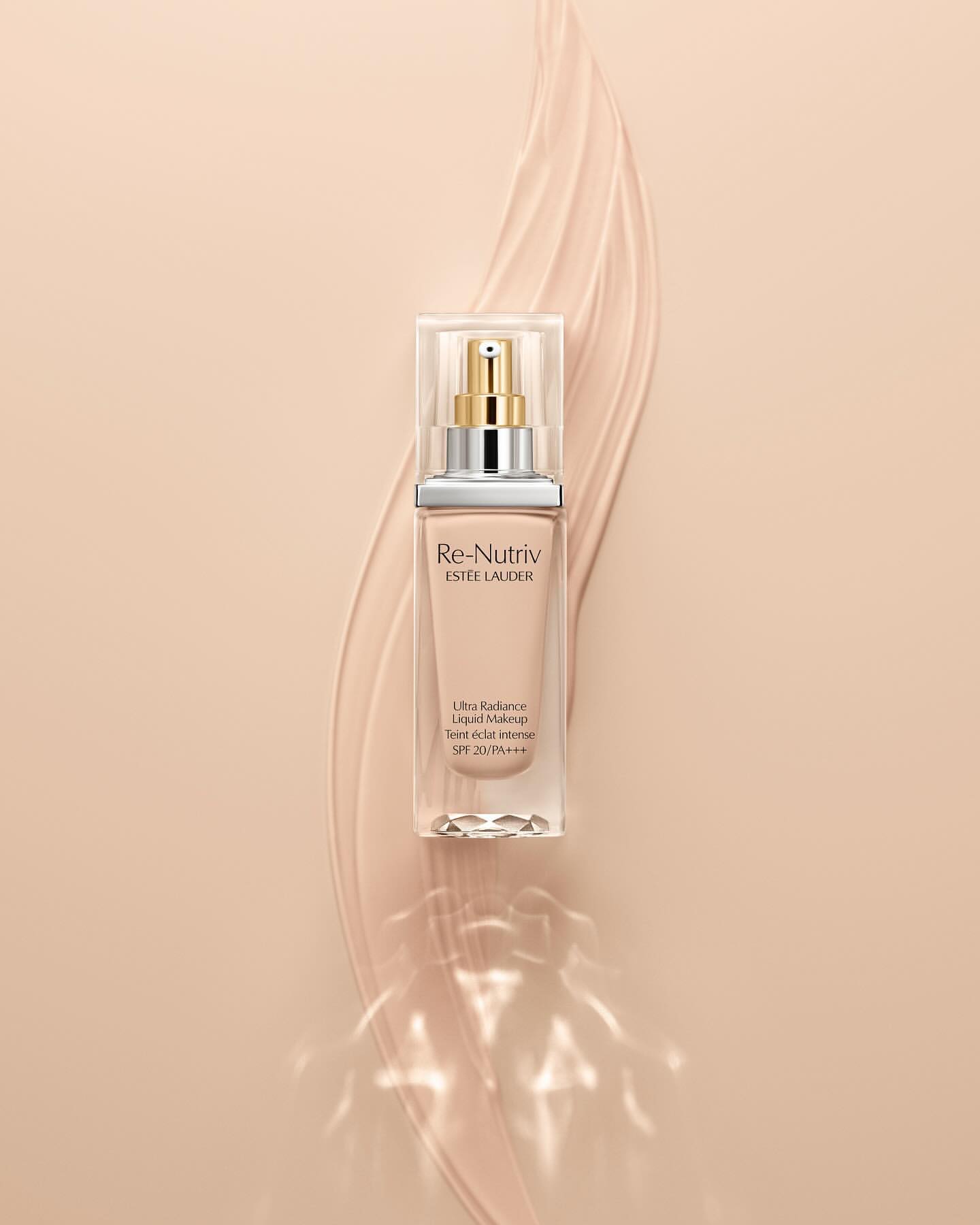Estee Lauder Re-Nutriv liquid makeup bottle on a cream-colored background with light beige makeup swipe accent.