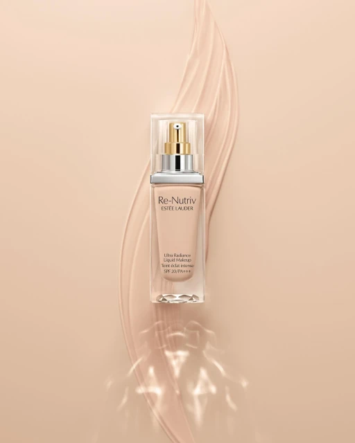 Estee Lauder Re-Nutriv liquid makeup bottle on a cream-colored background with light beige makeup swipe accent.