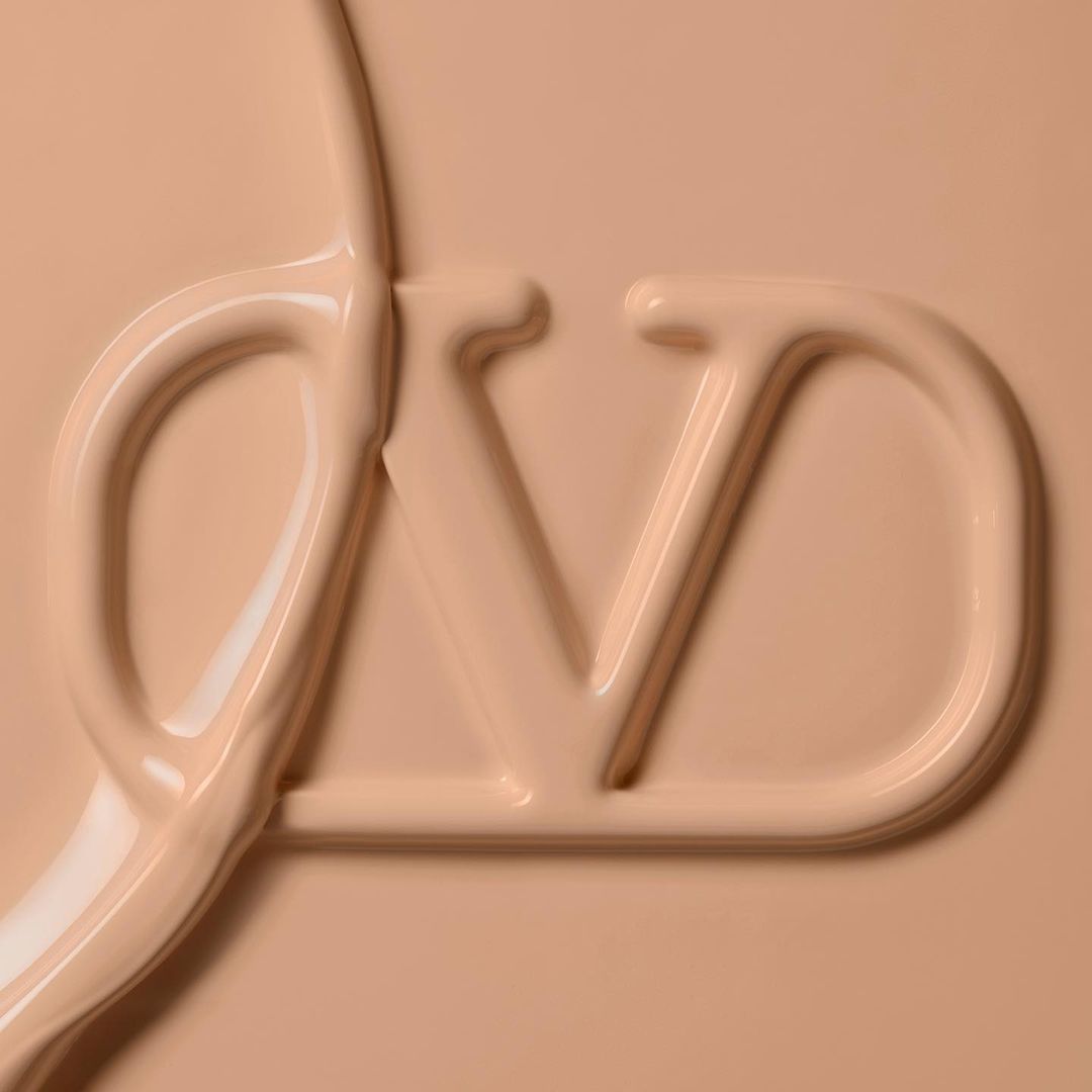 Close-up shot of beige-toned liquid cosmetic foundation with an embossed fashion logo visible on the surface, beauty-themed imagery.