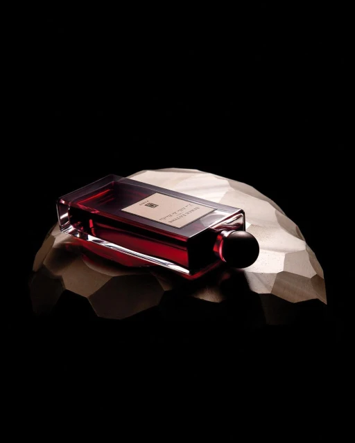 Red glass perfume bottle on a faceted gold surface against a dark background, product photography.
