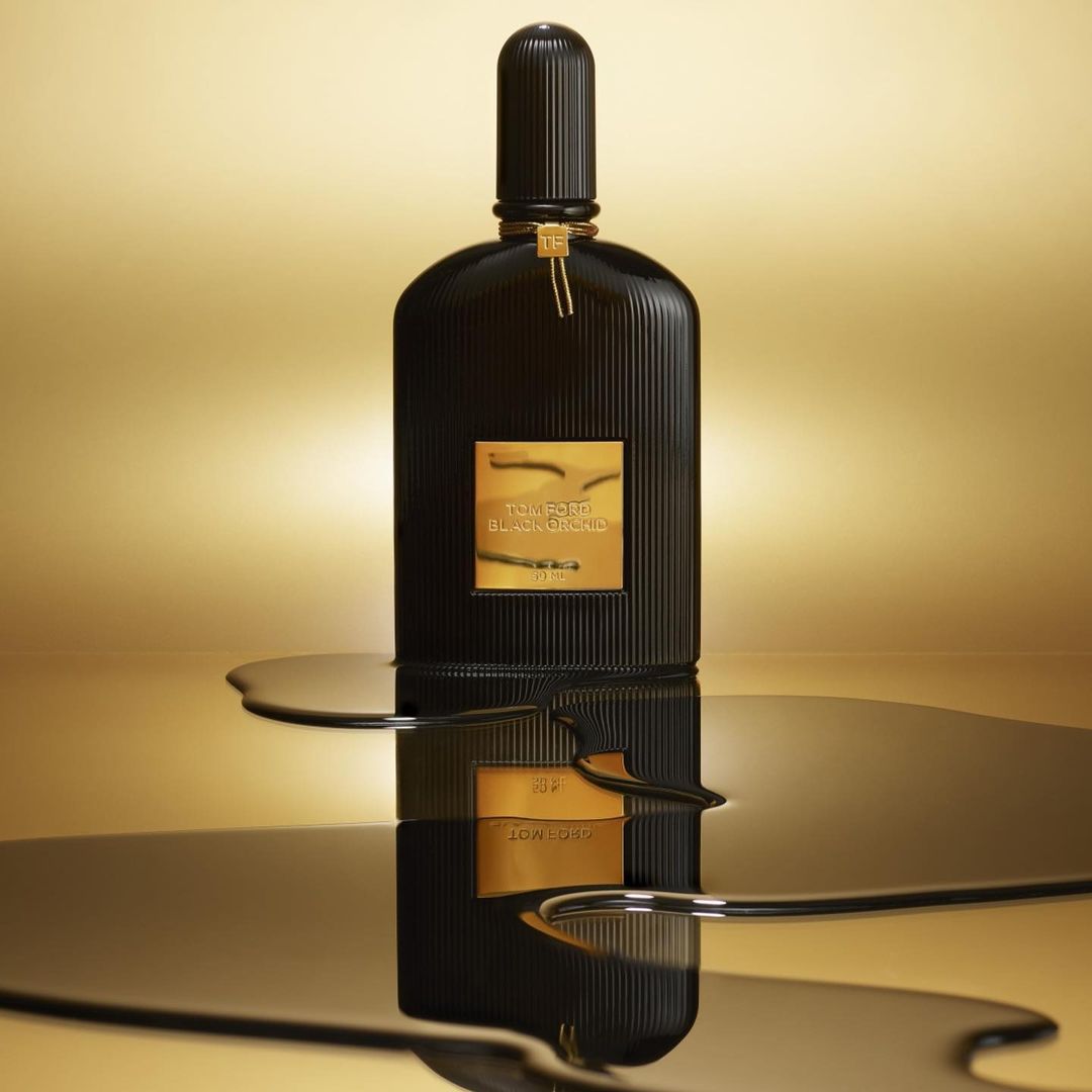 Black Tom Ford Black Orchid perfume bottle on a glossy surface with golden liquid spill, against a golden gradient background.