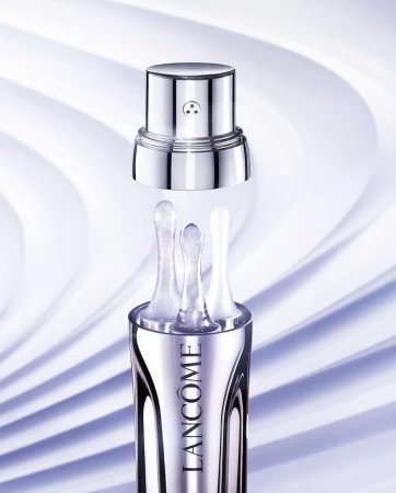 Close-up product shot of a silver Lancôme cosmetics bottle with three applicator tips against a pale purple swirling background