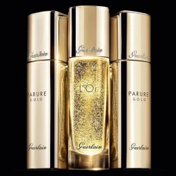 Three gold cosmetic bottles and perfume containers arranged vertically against a pure black seamless background.