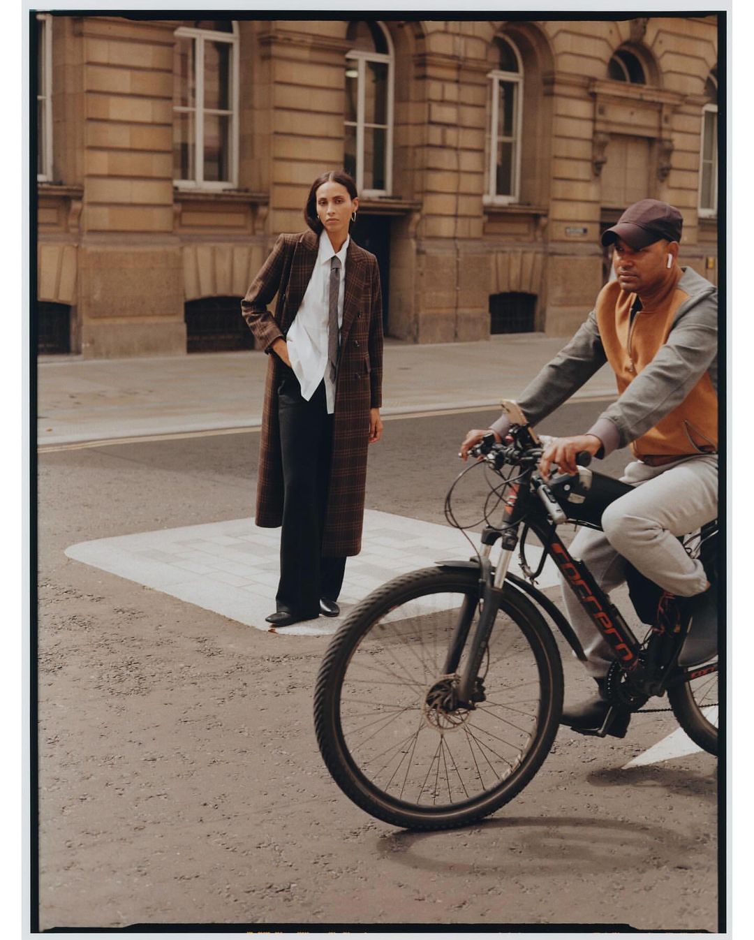 Stylish woman in coat with bicycle rider on street. Female fashion model poses in urban setting. Street style shoot in daylight.