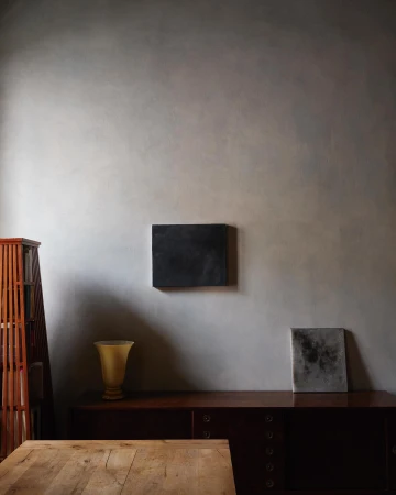 Interior view of a room featuring a wooden table, brown dresser, and wall art in shades of brown, grey and yellow with natural lighting.