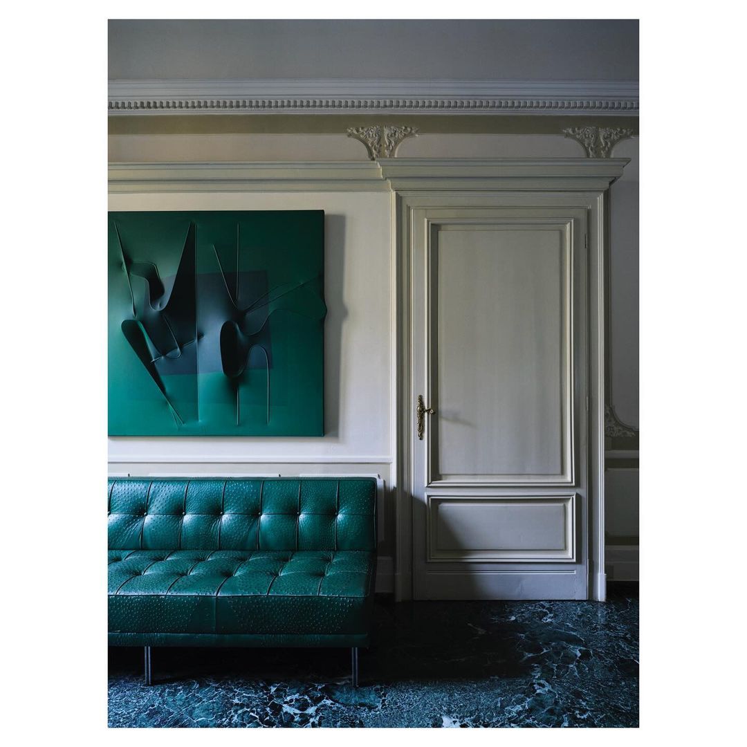 Emerald green leather tufted sofa, abstract art on wall, marble floor and white door in modern interior design living room.