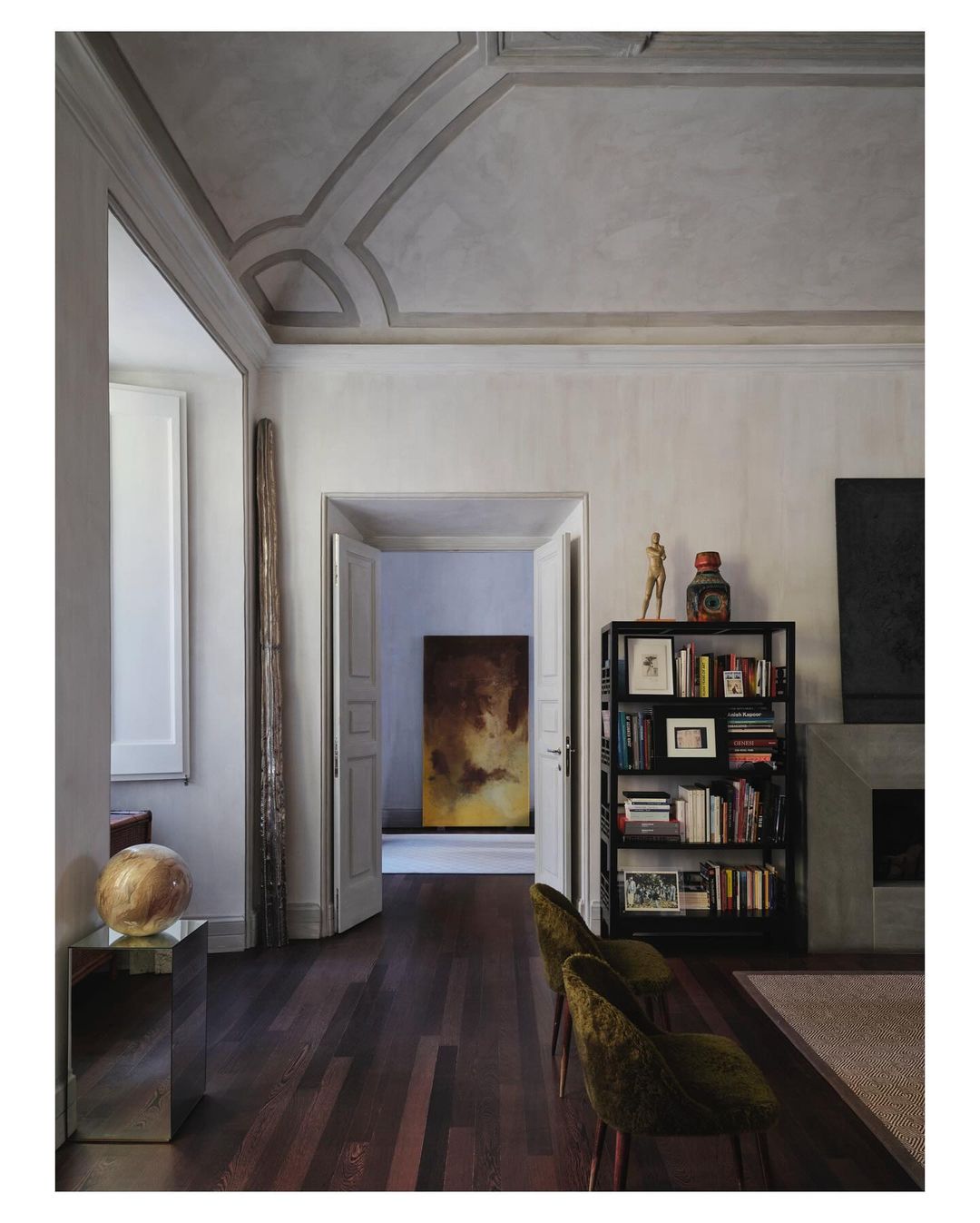 Interior view of a living room with hardwood floors, a fireplace, bookshelves, and decorative objects in a neutral color palette.