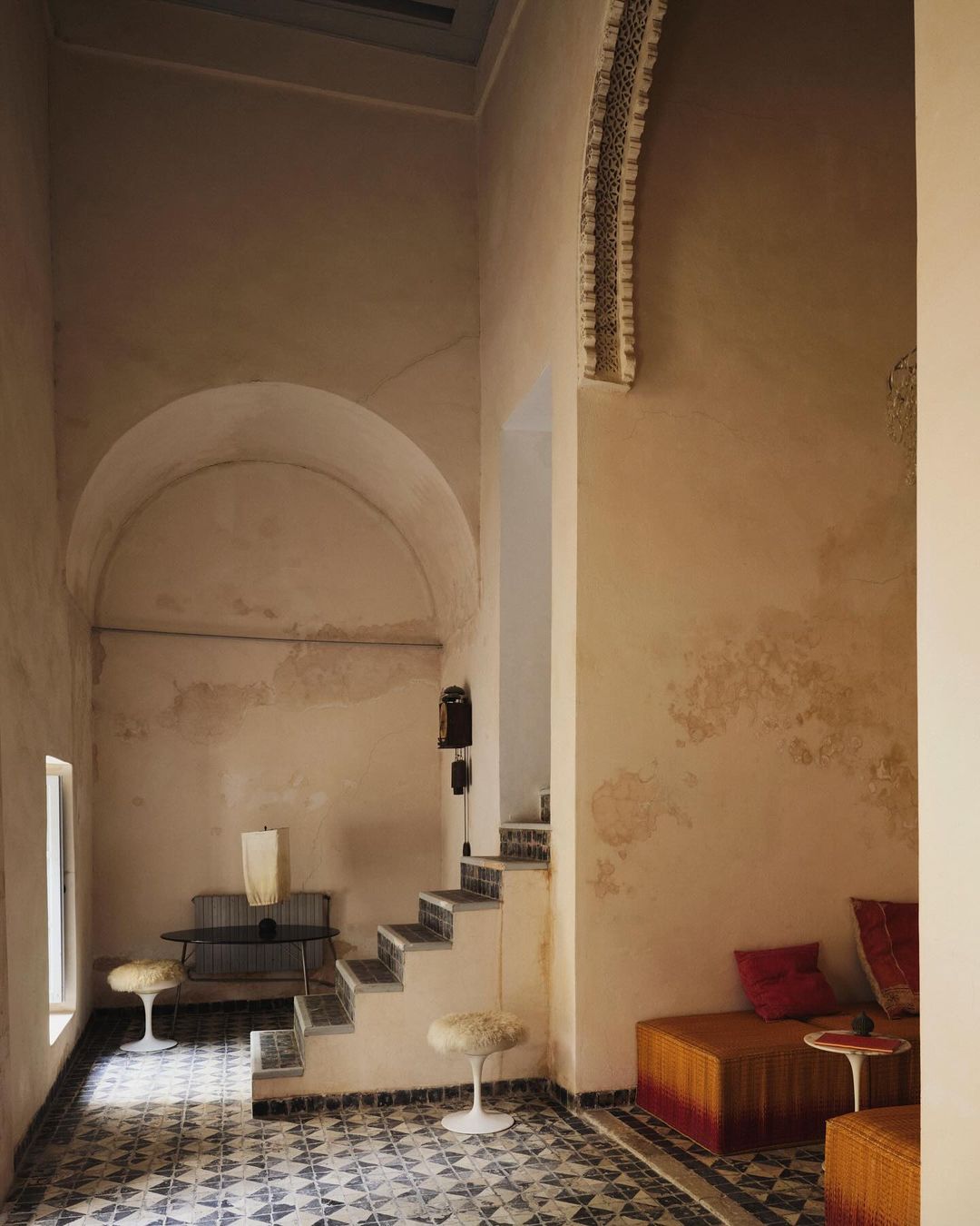Interior view of a room with a staircase, tiled floor, arched doorway, and built-in seating, featuring warm tones and natural light.