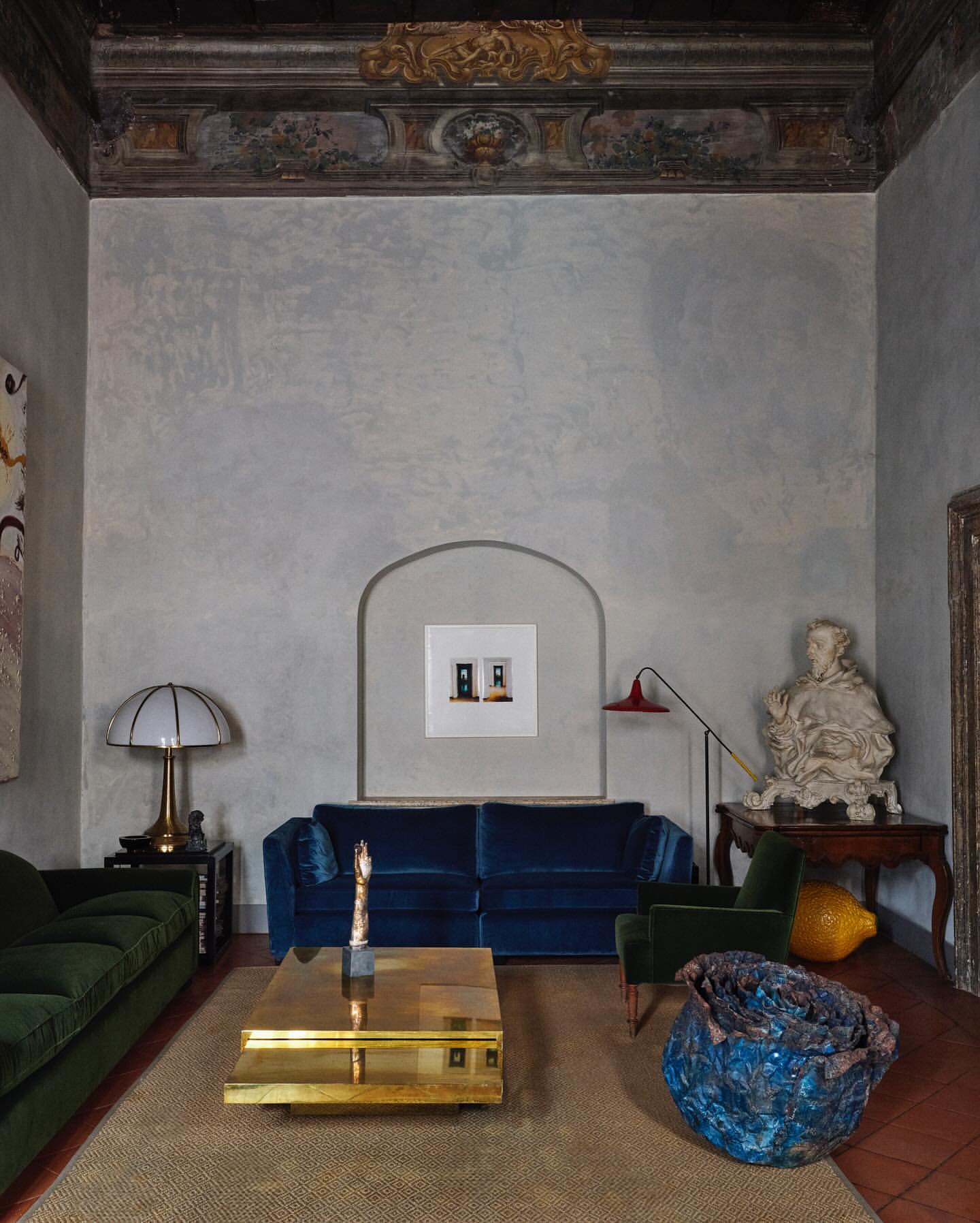 Luxurious interior features a blue velvet sofa, a gold coffee table, and classical decor in a spacious, elegant living room setting.