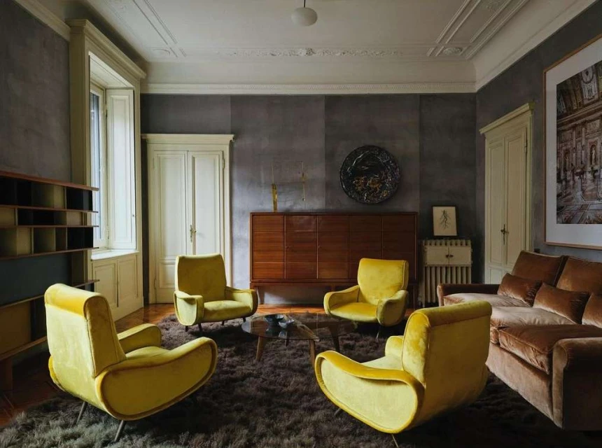 Living room interior with four yellow armchairs on a brown rug, a brown sofa, wooden cabinet, and white walls with white trim.