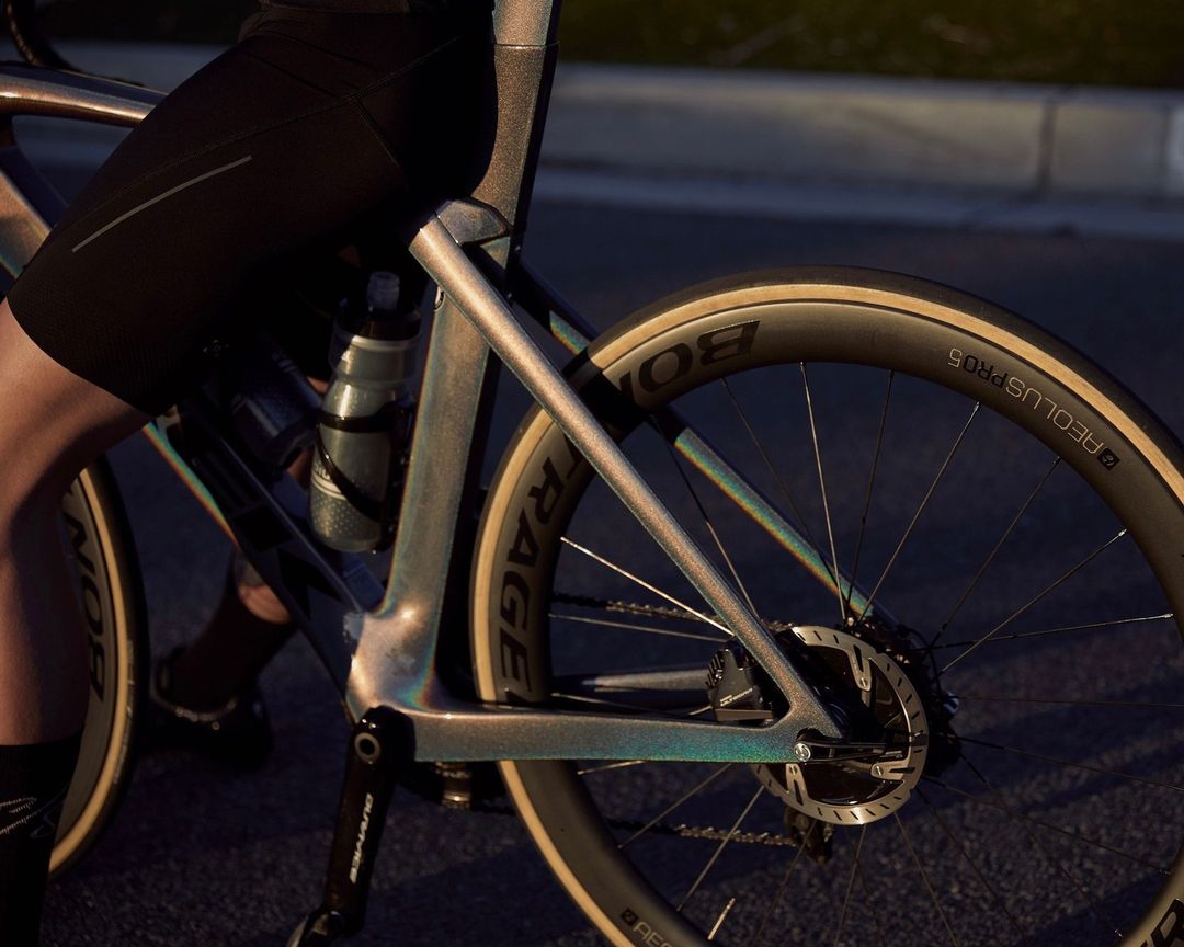 Person on a road bicycle with visible carbon fiber frame, wheels with logos, water bottle, and cycling apparel.