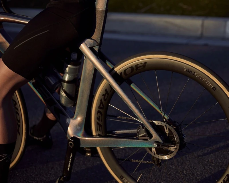Person on a road bicycle with visible carbon fiber frame, wheels with logos, water bottle, and cycling apparel.