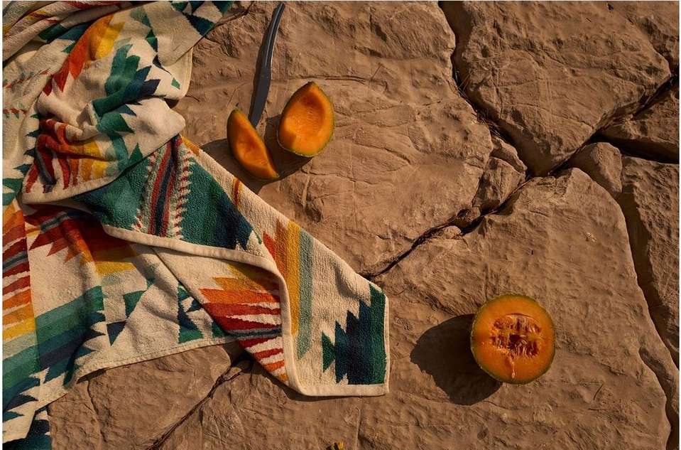 Still life of cantaloupe and a colourful patterned towel resting on a cracked rock surface, creating a summery, outdoorsy composition.