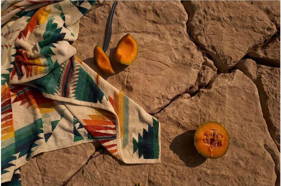 Still life of cantaloupe and a colourful patterned towel resting on a cracked rock surface, creating a summery, outdoorsy composition.