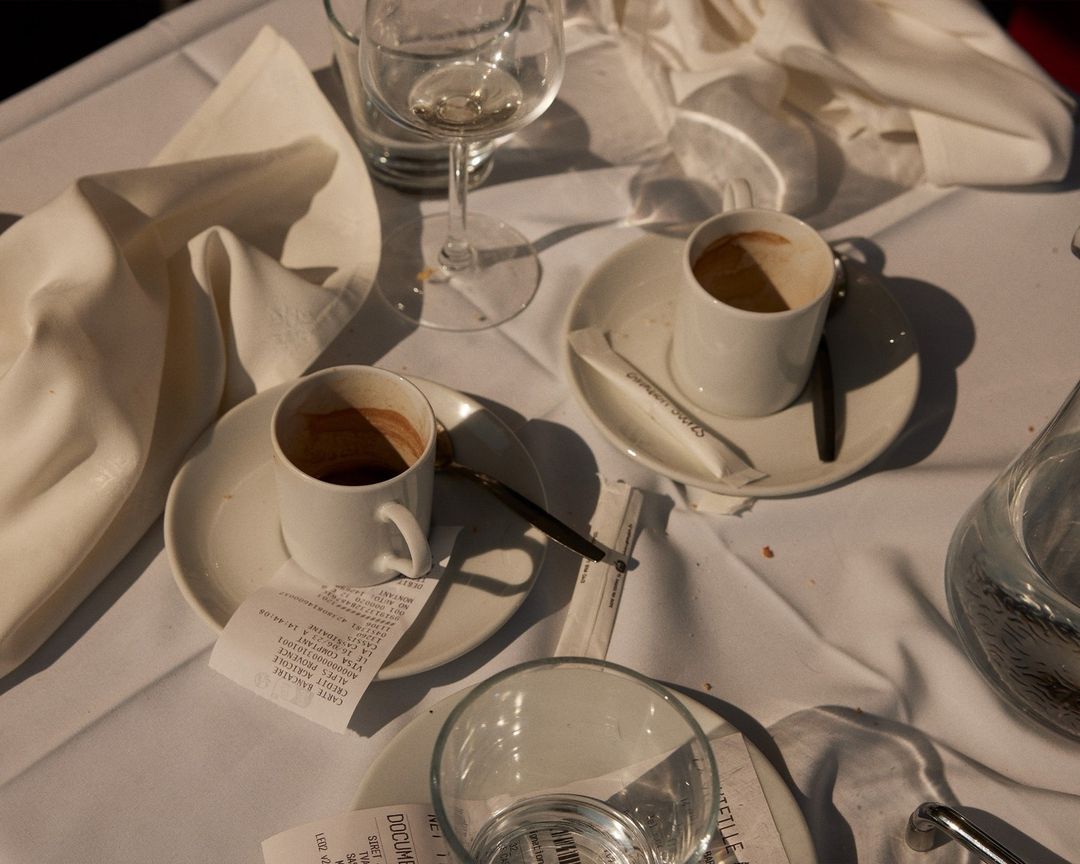 Two coffee cups and glasses on a white tablecloth in a restaurant setting with receipts and sugar packets, creating an intimate ambiance.