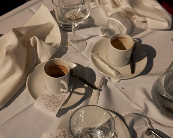 Two coffee cups and glasses on a white tablecloth in a restaurant setting with receipts and sugar packets, creating an intimate ambiance.