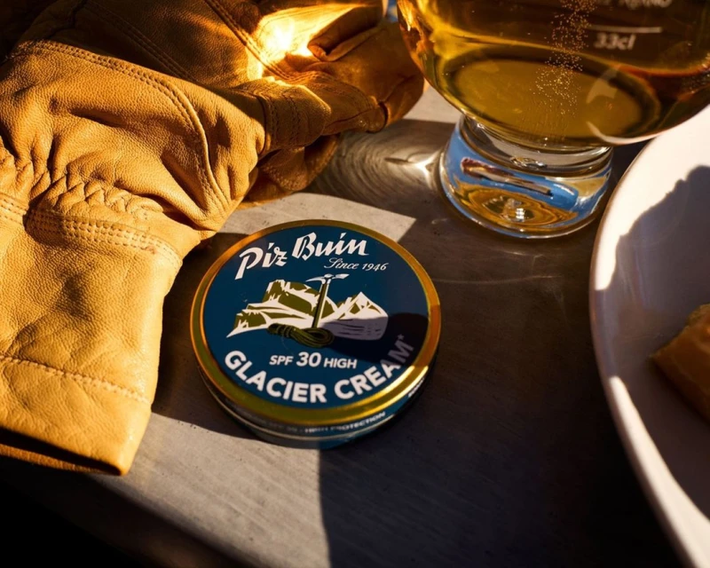 Close-up of Pirz Buin Glacier Cream, leather gloves, and a glass of beer, suggesting an après-ski theme for skincare.