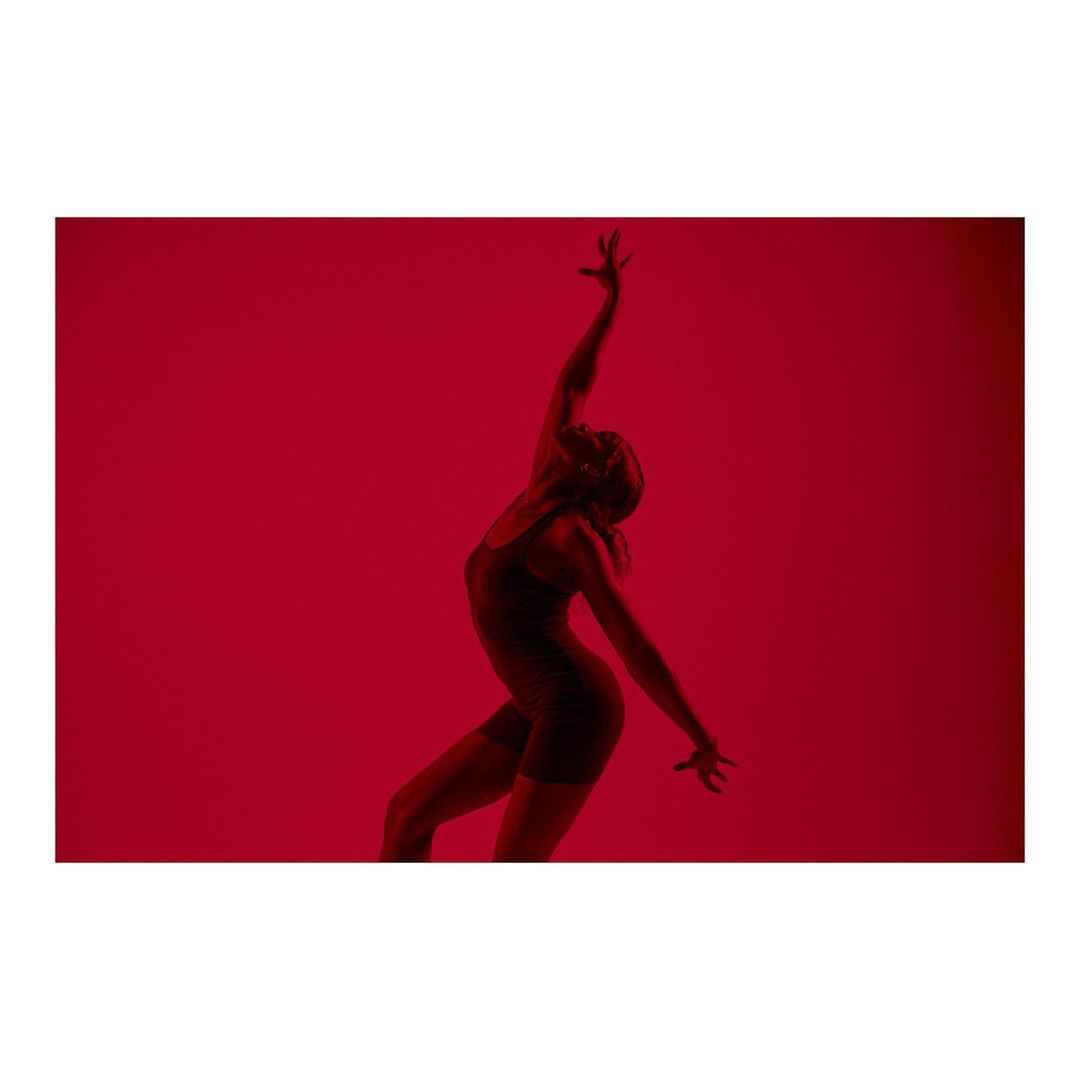 Silhouette of a female dancer against a vivid red backdrop, showcasing her expressive form and movement in a dramatic, monochromatic setting.