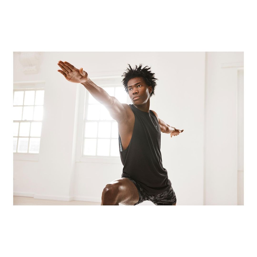 Athletic man in warrior pose with arms extended in bright studio. Healthy lifestyle, fitness, strength, flexibility, and wellness.