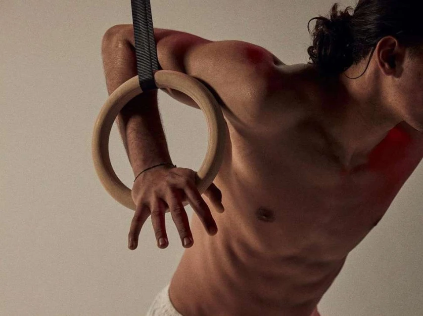 Athletic man on gymnastic rings demonstrates strength in a studio setting with neutral colors and athletic equipment, showing fitness and sport.