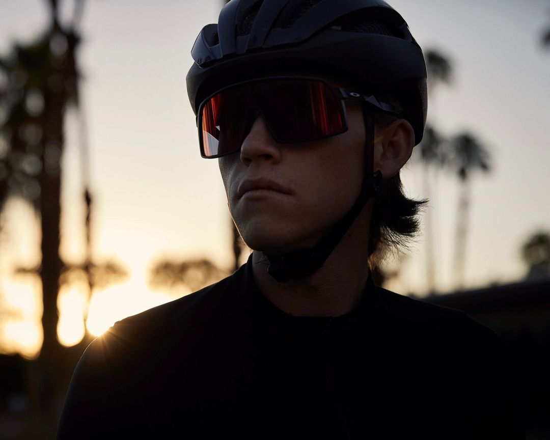 Profile of cyclist with helmet and sunglasses during golden hour, set against palm trees in warm, inviting light.