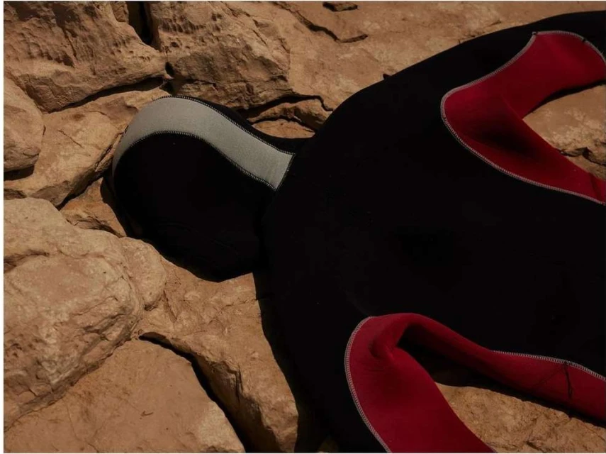 Close-up of a black and red wetsuit partially laying on tan and brown rocks in an outdoor setting under natural lighting conditions.