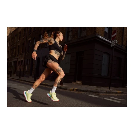 A tattooed woman in sportswear runs on a city street with buildings in the background, showcasing fitness and urban athleticism.