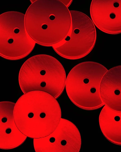 Pile of glossy red buttons with two holes on a black background creating a pattern of circular forms and strong contrasting colors.
