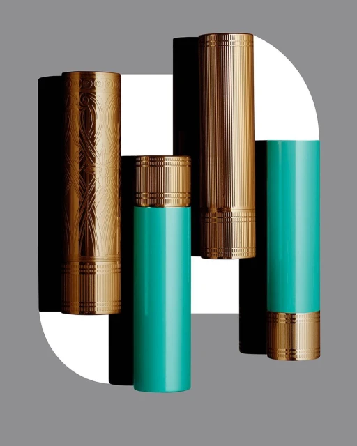 Five decorative bronze and teal cylinders stand against a geometric background of white, grey, and black shapes in a studio setting.