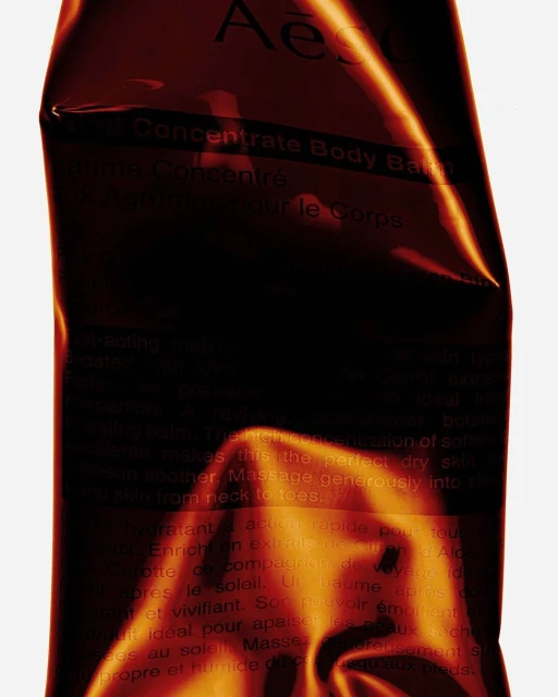 Concentrate Body Balm by Aesop. Close-up studio shot of product packaging in dark hues with light reflecting off the surface.