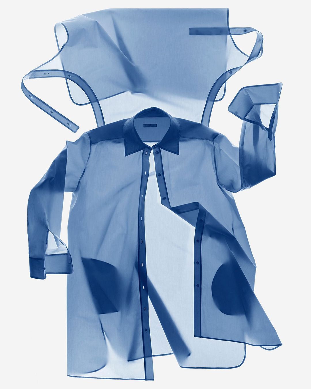 Blue-toned fashion studio shot of a sheer button-down shirt and translucent cape on a white backdrop, capturing airy elegance.