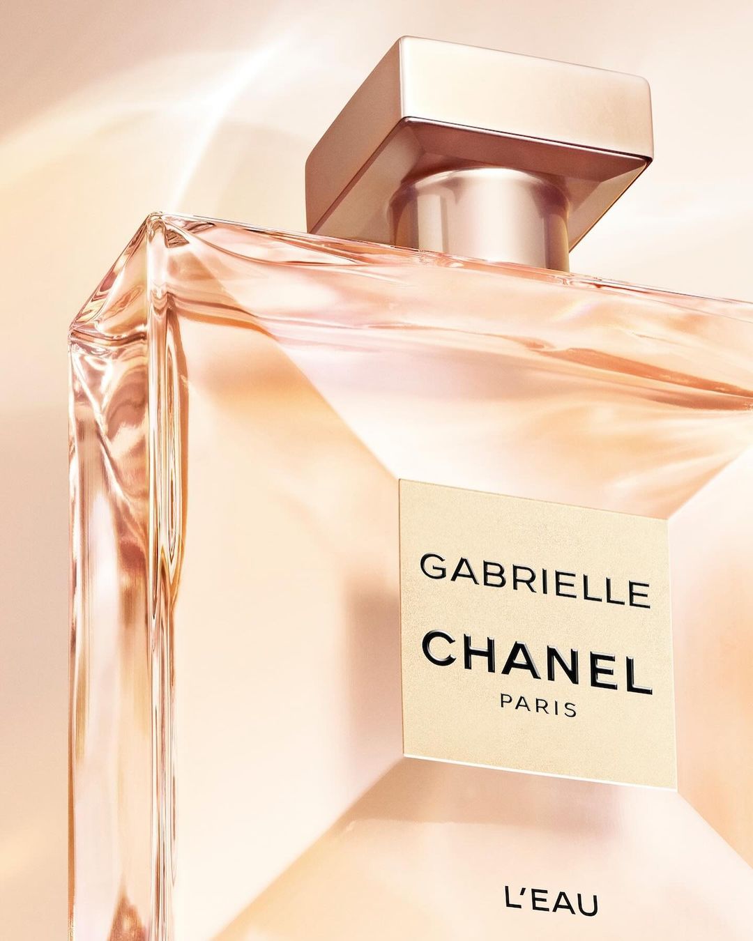 Close up view of a rectangular Gabrielle Chanel L'Eau perfume bottle with faceted glass against a soft warm gradient background.