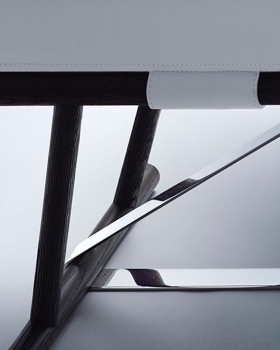 Close-up of a modern chair featuring dark wood legs, a chrome support bar, and white leather upholstery against a soft, neutral backdrop.