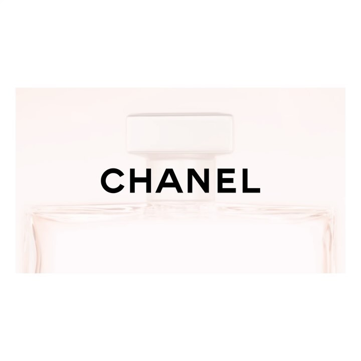 Close-up of a Chanel perfume bottle, showcasing its clear glass, white cap, and the iconic black brand name against a soft white background.