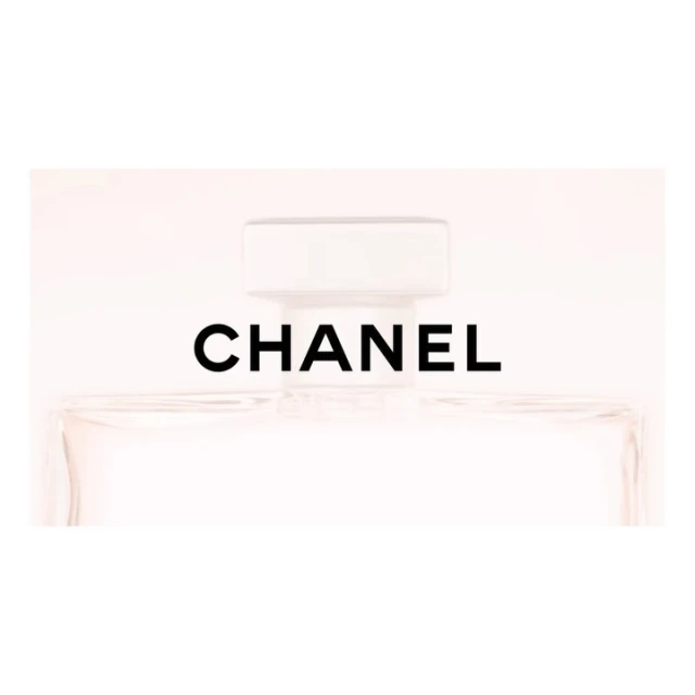Close-up of a Chanel perfume bottle, showcasing its clear glass, white cap, and the iconic black brand name against a soft white background.