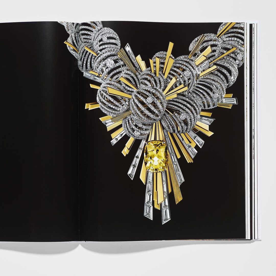 Intricate silver and gold necklace with yellow gem on black book page, luxurious jewelry design, high-fashion editorial, studio lighting.